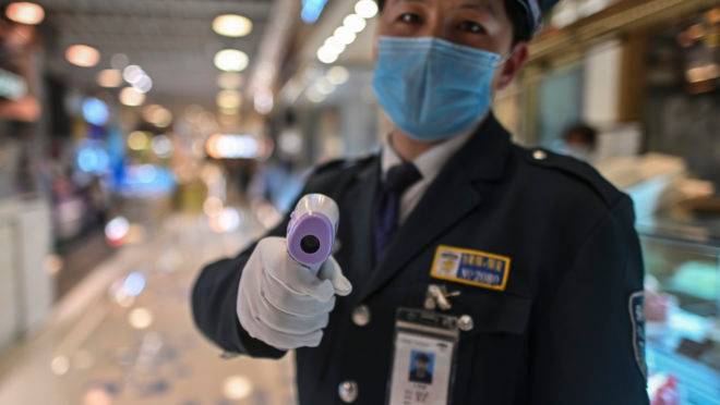 A guard wearing a facemask amid concerns over the spread of the COVID-19 novel coronavirus, holds a thermal gun to check the body temperature of visitors at the entrance of a restaurant area in Shanghai, on March 21, 2020. (Photo by Hector RETAMAL / AFP)