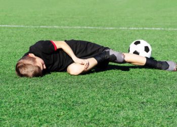 A young boy soccer player injured his leg during the match. Sufferer child football player and ball on the field. Kids injury in sport concept. Children's football school. Background. Copy space