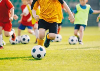 Football Training Camp. Football soccer children training class. Kids practicing football on grass field. Group of school children running and kicking soccer balls