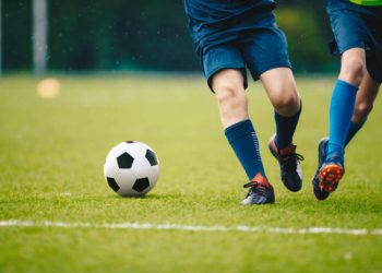 Two adult football players running and kicking a soccer ball. Legs of two young football players on a match. European football youth player legs in action