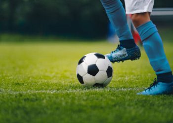 Close up of legs and feet of football player in blue socks and shoes running and dribbling with the ball. Soccer player running after the ball. Sports venue in the background